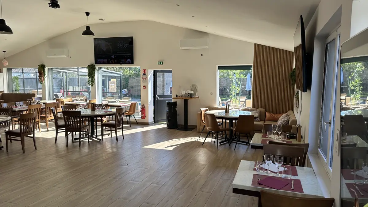 La salle en plein jour sous la charpente claire, les baies ouvertes sur la terrasse